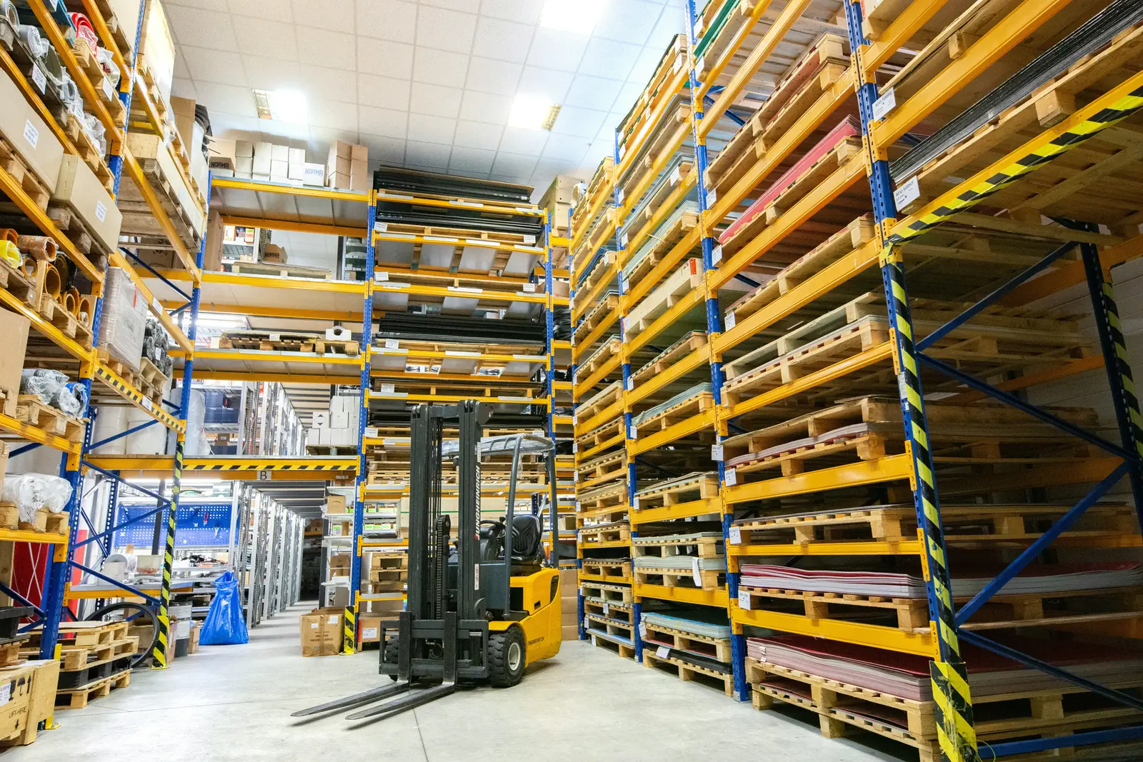 Forklift between tall racks of palletised stock
